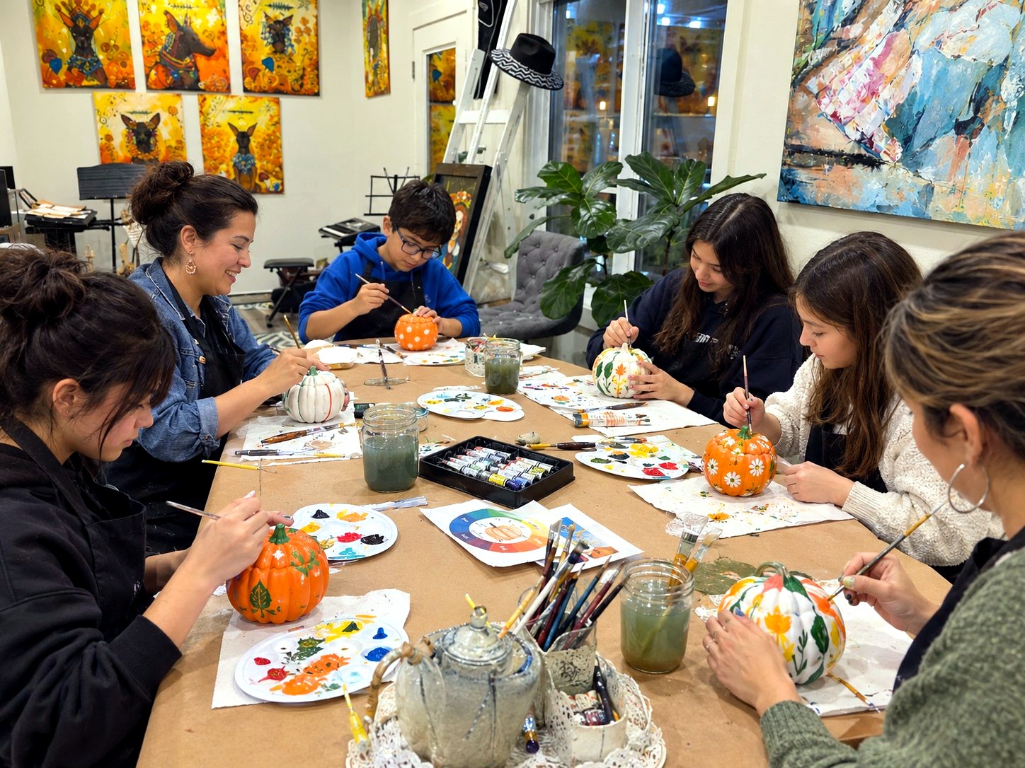People painting ceramic pumpkins together at a table in the studio